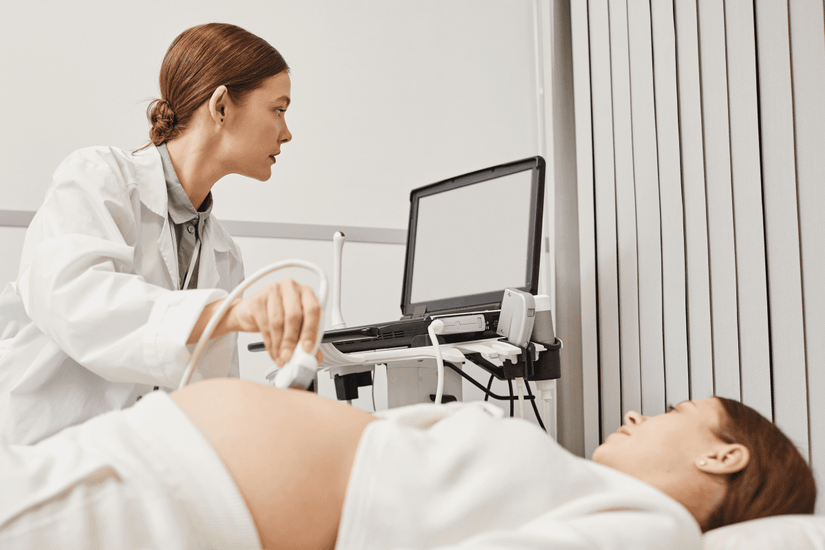 Caucasian female clinician performing a sonogram on a Caucasian female patient who is pregnant.