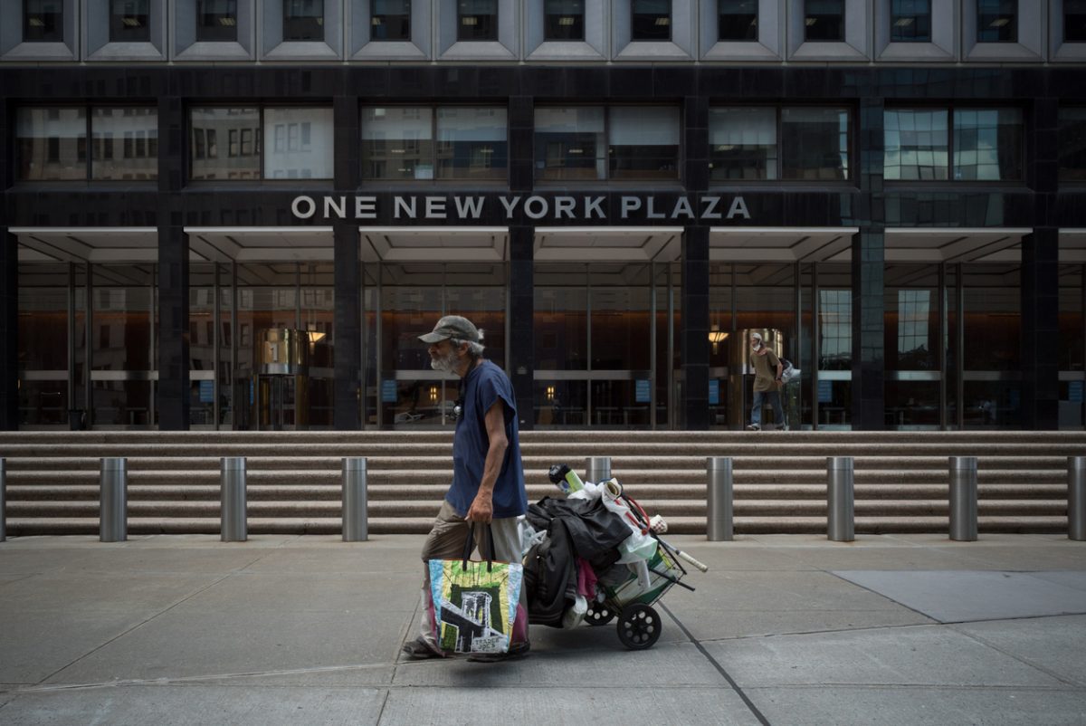 Manhattan, New York. July 07, 2020. A homeless man with his belongings walks in front of the entrance of One New York Plaza building. 1 New York Plaza is an office building in New York City's Financial District.
